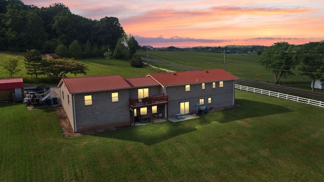 back of house featuring a rural view, fence, metal roof, and a yard