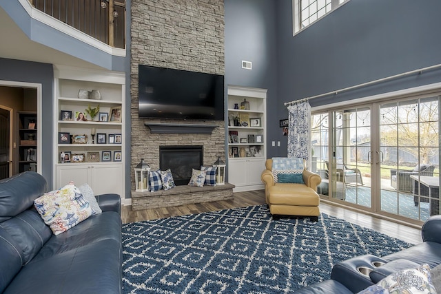 living room with built in shelves, visible vents, a high ceiling, a stone fireplace, and wood finished floors