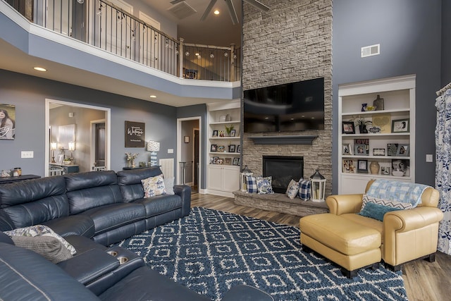 living room featuring built in shelves, visible vents, a stone fireplace, and wood finished floors