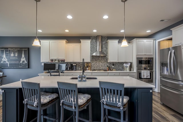 kitchen featuring dark wood-type flooring, a sink, appliances with stainless steel finishes, wall chimney range hood, and backsplash