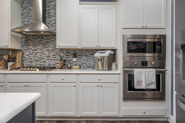 kitchen with tasteful backsplash, light countertops, appliances with stainless steel finishes, white cabinets, and wall chimney range hood