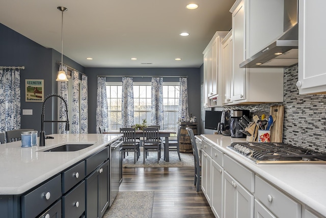 kitchen featuring wall chimney exhaust hood, stainless steel appliances, light countertops, white cabinetry, and a sink