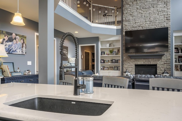 kitchen with built in shelves, pendant lighting, a fireplace, a towering ceiling, and a sink