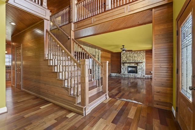 staircase with a fireplace, a towering ceiling, ceiling fan, wood walls, and wood finished floors