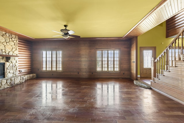 unfurnished living room with stairs, wood finished floors, a ceiling fan, and a stone fireplace