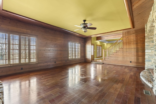 unfurnished living room featuring a wealth of natural light, visible vents, stairway, wood walls, and wood finished floors