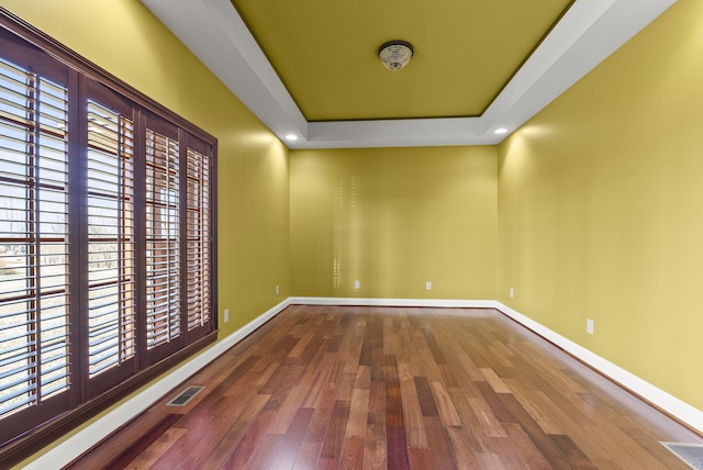 spare room featuring a tray ceiling, wood finished floors, visible vents, and baseboards