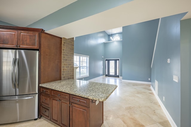 kitchen with baseboards, light stone countertops, a peninsula, freestanding refrigerator, and a towering ceiling