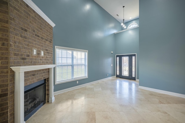 unfurnished living room featuring a healthy amount of sunlight, a brick fireplace, baseboards, and a towering ceiling