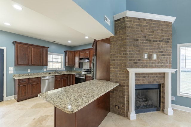 kitchen with light stone counters, a peninsula, a sink, under cabinet range hood, and appliances with stainless steel finishes