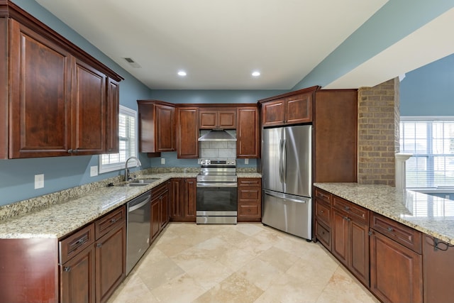 kitchen with under cabinet range hood, appliances with stainless steel finishes, light stone countertops, and a sink