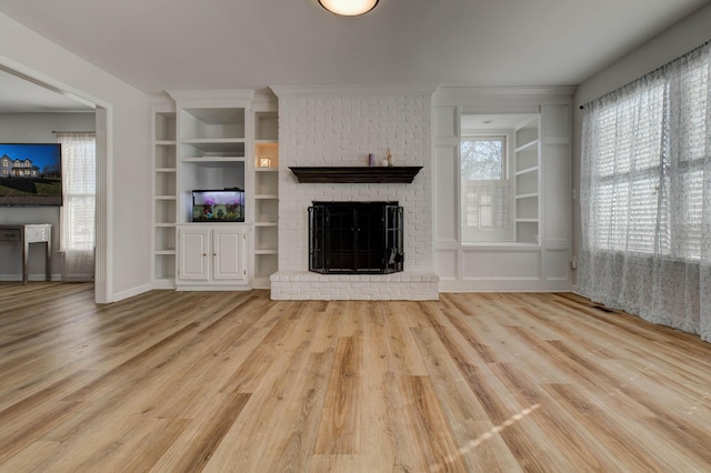 unfurnished living room with baseboards, a fireplace, built in features, and wood finished floors