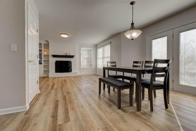 dining room with light wood finished floors, a fireplace, built in shelves, and baseboards