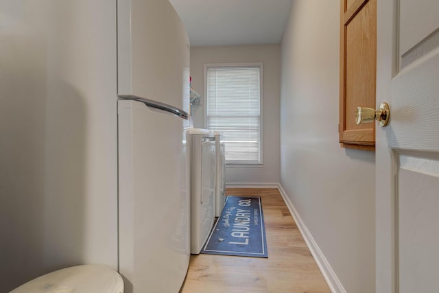 clothes washing area featuring light wood finished floors, washing machine and dryer, laundry area, and baseboards