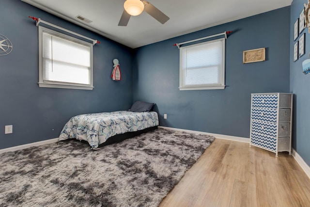 bedroom featuring a ceiling fan, visible vents, baseboards, and wood finished floors