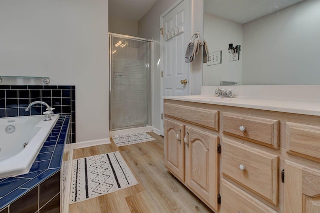 full bathroom featuring wood finished floors, vanity, baseboards, a bath, and a stall shower