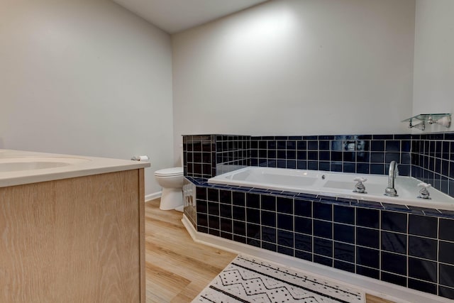 bathroom with toilet, wood finished floors, vanity, baseboards, and a bath