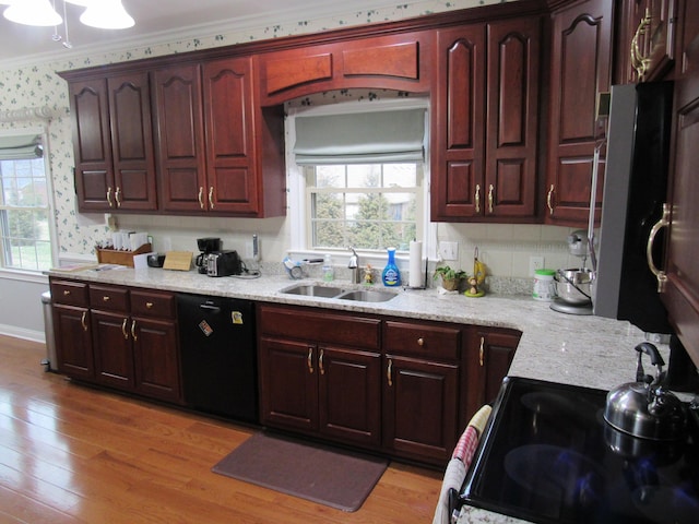 kitchen with light wood finished floors, wallpapered walls, ornamental molding, black appliances, and a sink