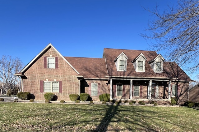 new england style home with brick siding, a porch, and a front yard