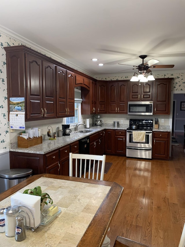 kitchen featuring wood finished floors, wallpapered walls, ornamental molding, a sink, and appliances with stainless steel finishes