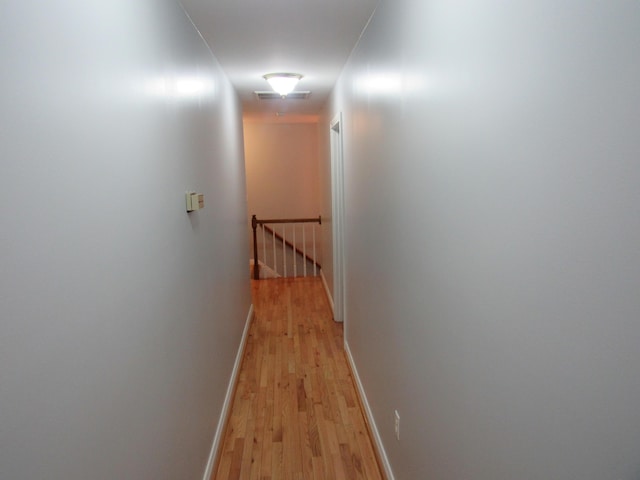 hallway featuring an upstairs landing, baseboards, visible vents, and light wood finished floors