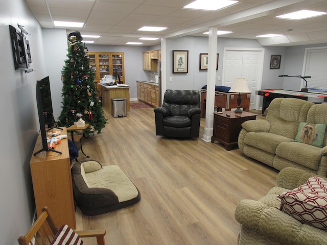 living room featuring a drop ceiling, baseboards, and light wood finished floors