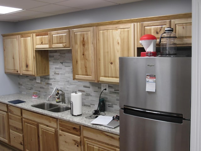 kitchen featuring light brown cabinetry, a sink, tasteful backsplash, freestanding refrigerator, and a paneled ceiling