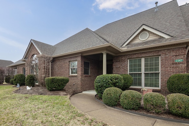 view of front facade with a front yard, brick siding, and roof with shingles