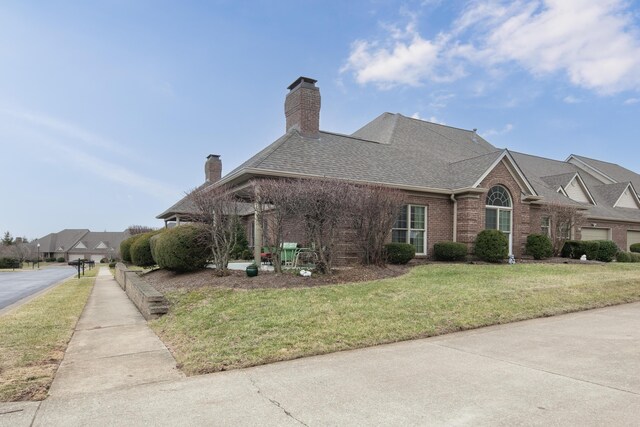 view of home's exterior featuring brick siding, a chimney, a shingled roof, and a lawn