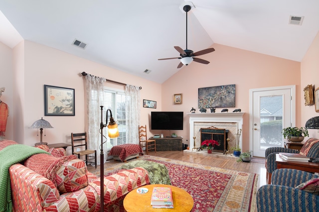 living area with a high end fireplace, visible vents, vaulted ceiling, and wood finished floors