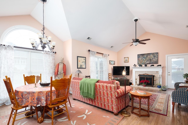 interior space featuring a fireplace with raised hearth, ceiling fan with notable chandelier, wood finished floors, and a healthy amount of sunlight