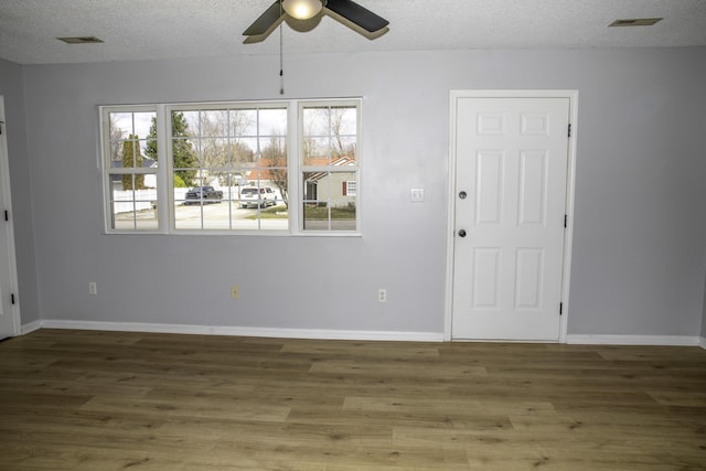 empty room with a textured ceiling, wood finished floors, visible vents, and baseboards