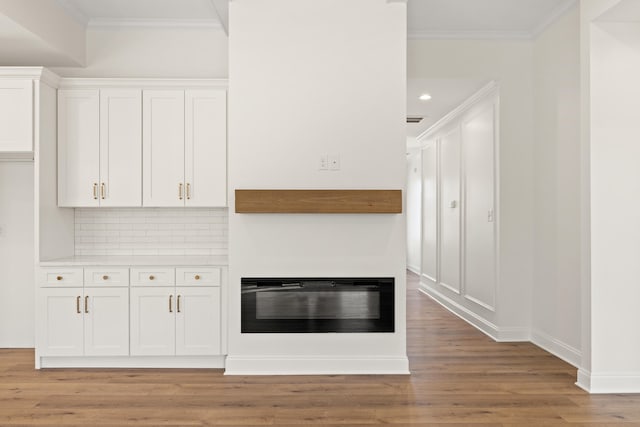 unfurnished living room featuring crown molding, recessed lighting, light wood-style floors, a glass covered fireplace, and baseboards