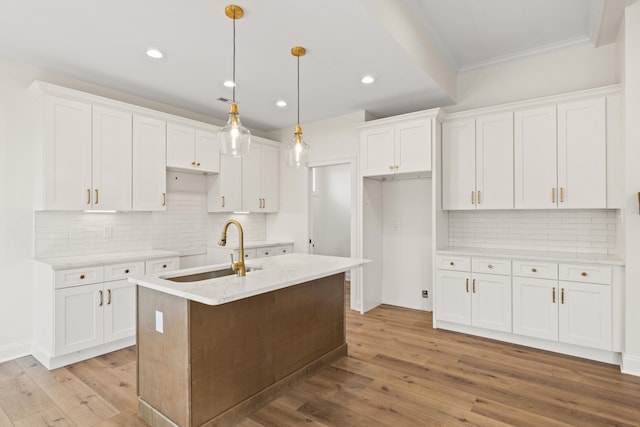 kitchen featuring light wood finished floors, a sink, a kitchen island with sink, and white cabinets