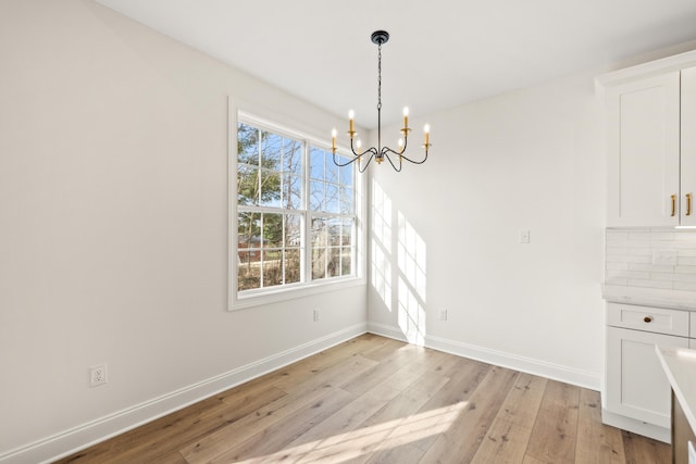 unfurnished dining area featuring light wood-type flooring, baseboards, and an inviting chandelier