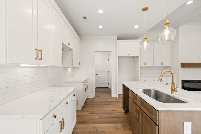 kitchen featuring visible vents, light stone counters, wood finished floors, a sink, and recessed lighting