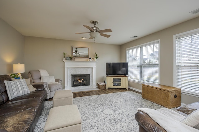 living area featuring baseboards, visible vents, a fireplace with flush hearth, ceiling fan, and wood finished floors