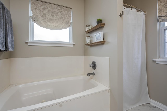 bathroom with marble finish floor, baseboards, and a bath