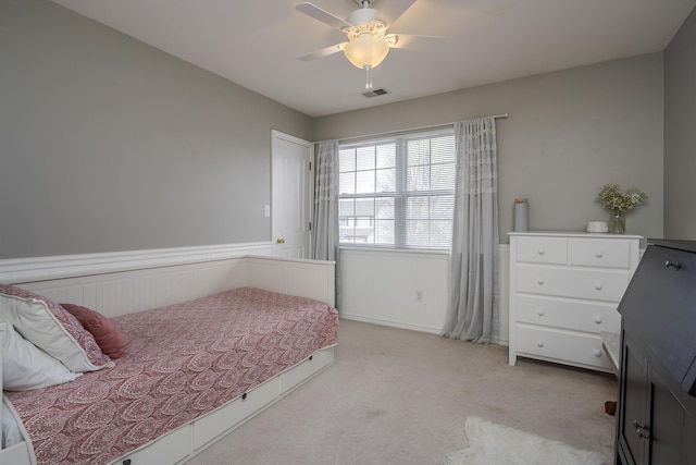 bedroom with a wainscoted wall, visible vents, a ceiling fan, and light colored carpet