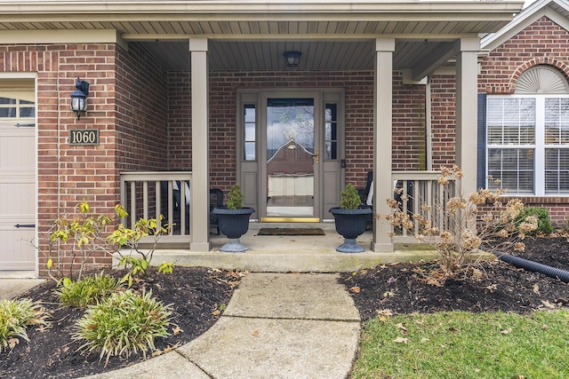 view of exterior entry with a garage, covered porch, and brick siding