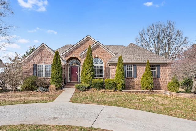 view of front of house featuring a shingled roof, a front yard, and brick siding