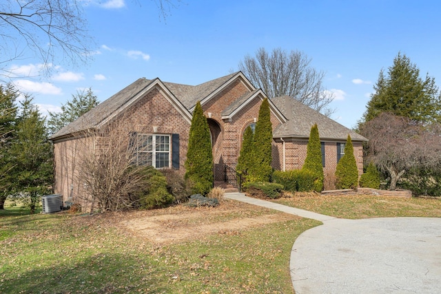 view of front facade with a shingled roof, central AC unit, a front lawn, and brick siding