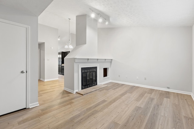 unfurnished living room featuring a textured ceiling, light wood-type flooring, a glass covered fireplace, and baseboards