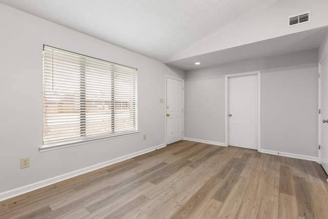 spare room featuring lofted ceiling, visible vents, baseboards, and wood finished floors