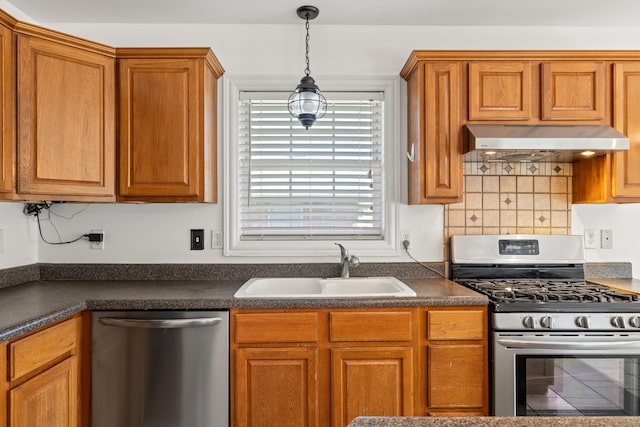 kitchen featuring dark countertops, under cabinet range hood, brown cabinets, stainless steel appliances, and a sink