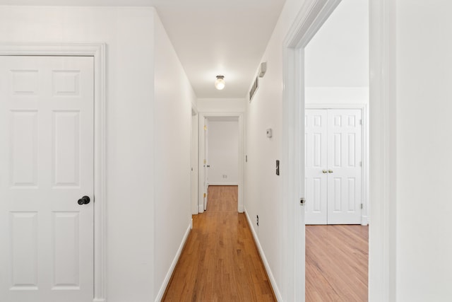 hall featuring visible vents, baseboards, and light wood finished floors