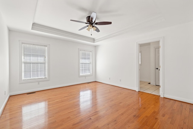 spare room featuring light wood-type flooring, a tray ceiling, visible vents, and crown molding