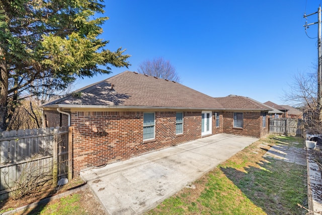 view of front of home featuring fence, a patio area, brick siding, and a shingled roof