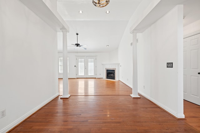 unfurnished living room with baseboards, ceiling fan, decorative columns, a tile fireplace, and hardwood / wood-style flooring