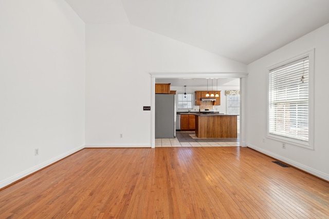 unfurnished living room featuring visible vents, baseboards, light wood-style floors, and vaulted ceiling